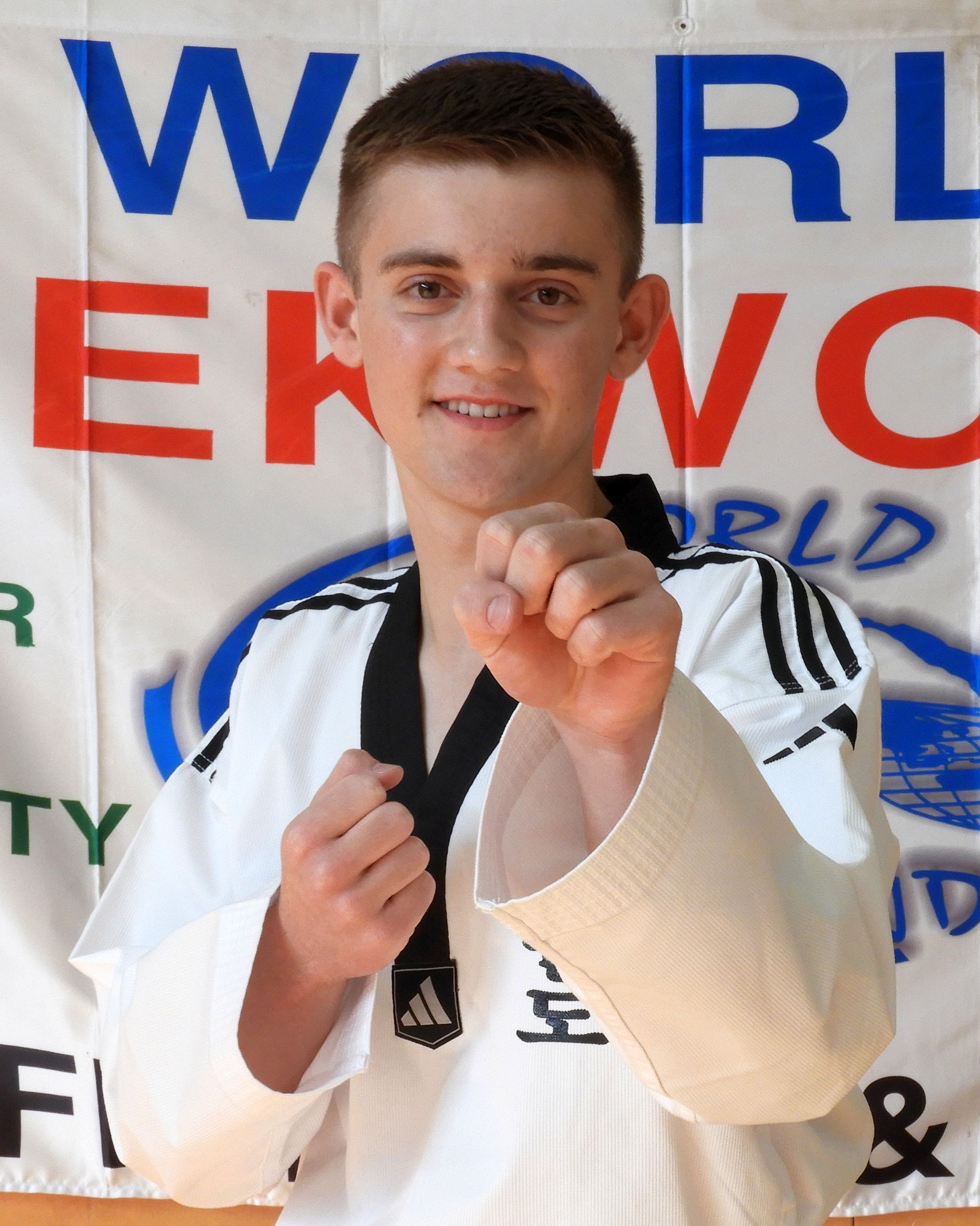 Alex Short in world taekwondo formal uniform, standing happily in a guarding block position showing confidence.