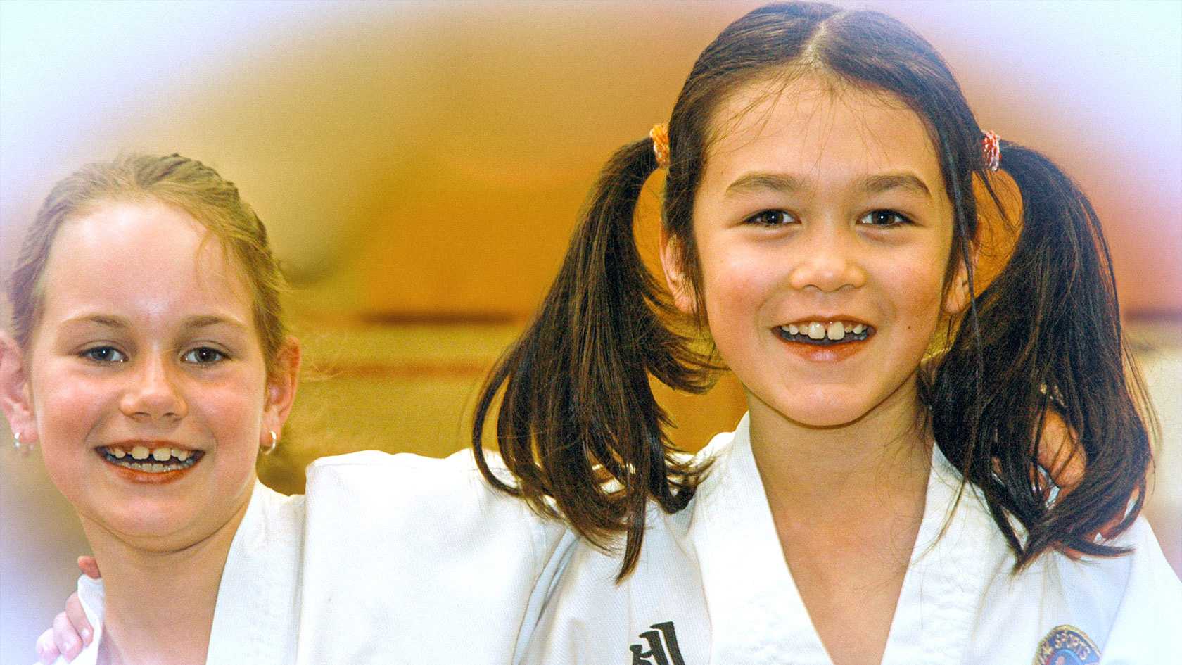 Two young girls in Taekwondo uniforms smiling and laughing together.
